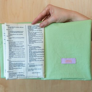 May include: A light green book cover with a book inside, held open by a hand. The book pages are visible, with text from a play. A small, rectangular label with the text "pretend bookshop" is on the cover.