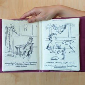 May include: A fabric book with illustrations and text from "Cried and Prejudice". The book has a purple cover and cream-colored pages with black and white drawings. The text includes quotes from the novel.
