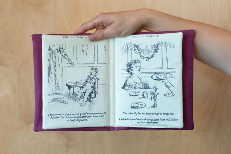 May include: A fabric book with illustrations and text from "Cried and Prejudice". The book has a purple cover and cream-colored pages with black and white drawings. The text includes quotes from the novel.