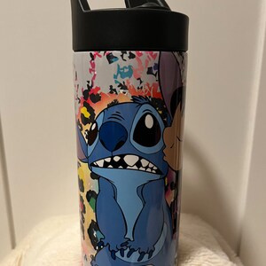 May include: A stainless steel water bottle with a black lid and handle. The bottle features a colorful abstract design with a cartoon image of Stitch from Lilo & Stitch.