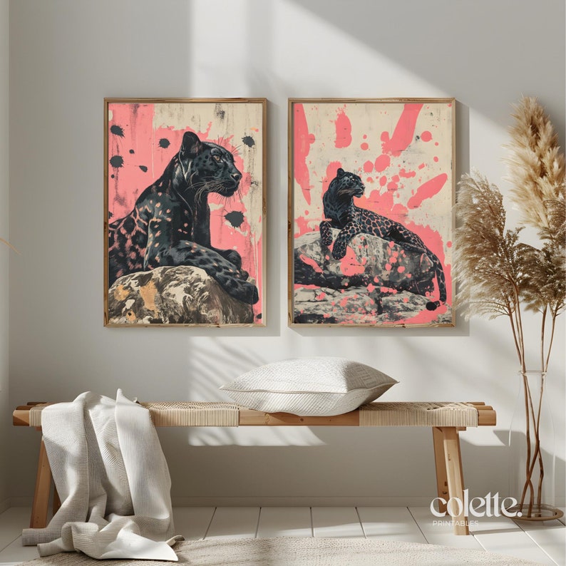 May include: Two black panther illustrations on a pink background with white paint splatters. The panthers are in different poses, one is sitting and the other is lying down. The illustrations are framed and hanging on a wall.