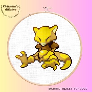 Könnte beinhalten: Kreuzstichmuster eines gelben und braunen Pokemon-Charakters auf weißem Aida-Stoff. Der Charakter ist ein fuchsartiges Wesen mit einem eingerollten Schwanz und einem geschlossenen Auge.