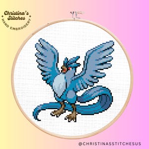 May include: Cross-stitch embroidery hoop featuring a blue and white pixelated image of a bird with a long tail, resembling a mythical creature. The hoop is made of wood and has a white background.