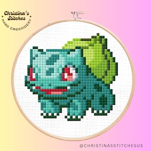 May include: A cross-stitch embroidery hoop with a green and blue pixelated image of a Pokemon character, Bulbasaur, with the text "Christina's Stitches Hand Embroidery" at the top.