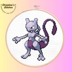 May include: A cross-stitch embroidery of the Pokémon Mewtwo, in shades of purple and gray, set in a wooden hoop. The design features the character in a dynamic pose. The text "Christina's Stitches" is visible at the top of the hoop.