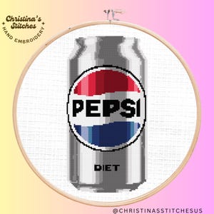 Puede incluir: Un aro de bordado blanco con un diseño de punto de cruz de una lata plateada de Pepsi Light. La lata tiene el logotipo de Pepsi en rojo, blanco y azul.