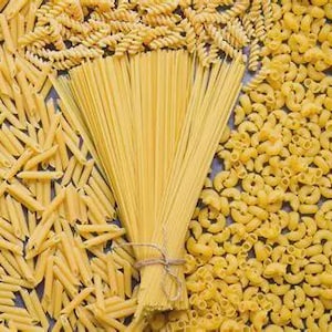 Puede incluir: Vista aérea de varias formas de pasta cruda. Penne, fusilli y macarrones rodean un manojo de espaguetis atados con hilo. La pasta es de color amarillo brillante.