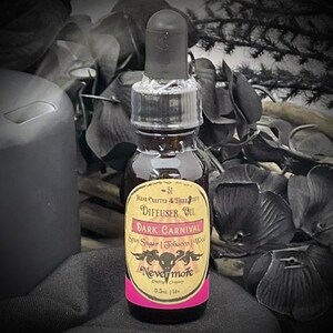 May include: A dark brown glass bottle of "Dark Carnival" diffuser oil with a black dropper. The label is yellow with pink accents and features the text "Nevermore Company". The bottle contains 0.5 fl oz.