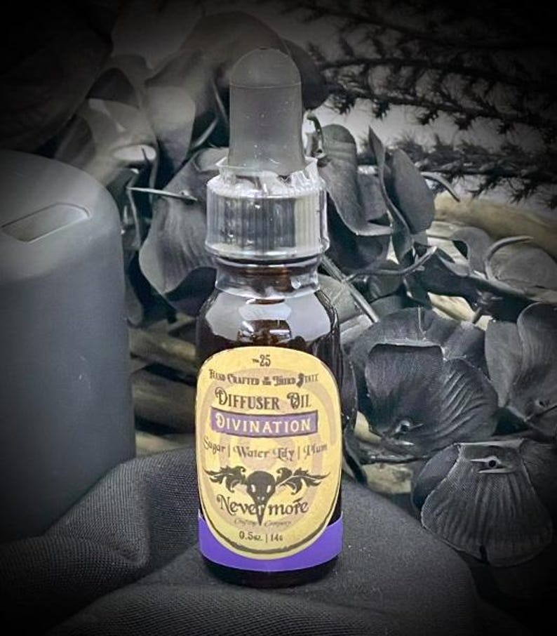 May include: A dark glass bottle with a dropper top, labeled "Diffuser Oil Divination" with the brand "Nevermore." The label includes ingredients: Sugar, Water Lily, and Plum. The bottle contains 0.5 fl oz.