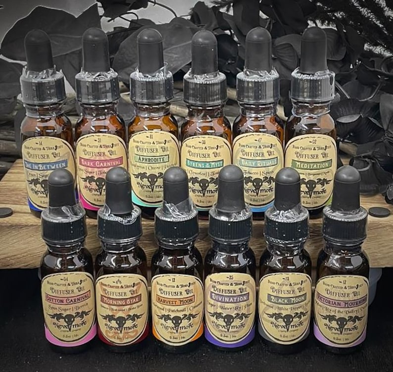 May include: A collection of brown glass diffuser oil bottles with black droppers. Each bottle has a label with a unique name, such as "Dark Carnival" and "Victorian Mourning." The labels feature a skull and crossbones design. The bottles are arranged on a wooden surface.