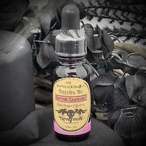 May include: A small, dark glass bottle of diffuser oil with a black dropper. The label reads "Cotton Carnival" and "Nevermore". The label is yellow with pink accents and features a skull and floral design. The bottle contains 0.5 oz (14 ml) of oil.