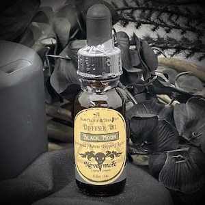 May include: A dark brown glass diffuser oil bottle with a black dropper. The label reads "Black Moon" and "Nevermore". The bottle contains 0.5 oz / 14 ml of oil. The background includes black flowers and a black candle.