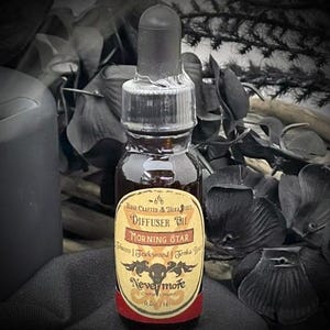 May include: A small glass bottle of diffuser oil with a black dropper. The label reads "Morning Star" and "Nevermore". The oil is dark brown, and the label has a vintage design with a skull and raven. The bottle contains 0.5 fl oz.