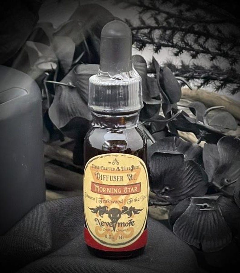 May include: A small glass bottle of diffuser oil with a black dropper. The label reads "Morning Star" and "Nevermore". The oil is dark brown, and the label has a vintage design with a skull and raven. The bottle contains 0.5 fl oz.