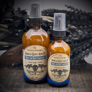 Peut inclure: Deux flacons en verre ambr&eacute; avec des vaporisateurs noirs et des &eacute;tiquettes. Les &eacute;tiquettes sont de couleur cr&egrave;me avec du texte noir qui indique "Hand Crafted Third State Home & Linen Spray The In Between Ocean | Sage | Ozone Nevermore Crafting Company" et la taille du flacon en onces et en millilitres. Le plus petit flacon est de 2 oz et le plus grand de 4 oz. Les flacons sont pos&eacute;s sur une surface en bois.