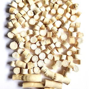 May include: A collection of small, light-colored wooden pieces, cut into various shapes and sizes, including cylinders and rectangular blocks. The pieces are scattered on a white surface, showcasing their natural wood grain.