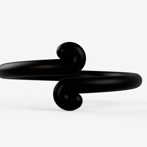 May include: A black ring with a unique design. The ring features a smooth, curved band that wraps around the finger, with two rounded, swirling accents. The ring is made of a solid, dark material and is set against a white background.