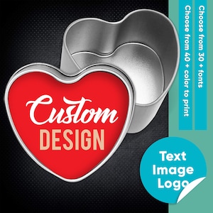 Op de afbeelding: Een zilveren hartvormige tin met een rood deksel. Het deksel heeft een wit ontwerp met de tekst "Custom DESIGN".