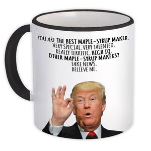 May include: White ceramic mug with a black handle and rim. The mug features a portrait of a man and text that reads, "YOU ARE THE BEST MAPLE-SYRUP MAKER. VERY SPECIAL, VERY TALENTED. REALLY TERRIFIC. HIGH IQ. OTHER MAPLE-SYRUP MAKERS? FAKE NEWS. BELIEVE ME."