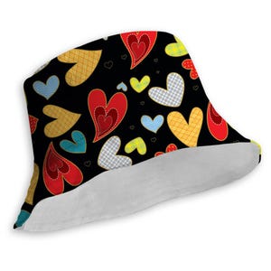 Op de afbeelding: Een zwarte bucket hat met een kleurrijk patchwork hartpatroon. De harten zijn in tinten rood, geel, blauw en groen. De hoed heeft een witte rand.