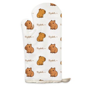 Peut inclure: Un gant de cuisine blanc avec un motif répété de capybaras de dessin animé en nuances de marron. Le nom "Elizabeth" est écrit en cursive entre les illustrations de capybaras. Le gant a une boucle pour l'accrocher et est fait d'un tissu texturé.