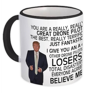 May include: White ceramic mug with a black handle and rim. The mug features a photo of a man in a suit and text that reads "YOU ARE A REALLY, REALLY GREAT DRONE PILOT THE BEST. REALLY TERRIFIC JUST FANTASTIC...BELIEVE ME."