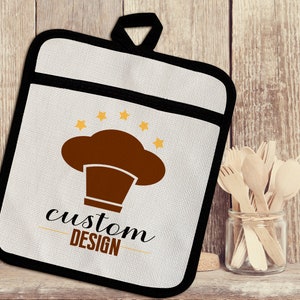 May include: White cotton pot holder with a black border. The pot holder has a brown chef hat with five yellow stars above it. The text "custom DESIGN" is printed below the chef hat.