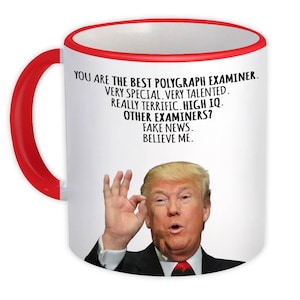 May include: White ceramic mug with a red handle and rim. The mug features text that reads "YOU ARE THE BEST POLYGRAPH EXAMINER" and a picture of a man. The mug is a novelty item.