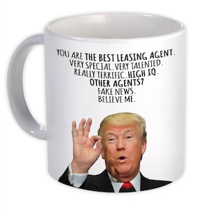 May include: White ceramic mug with a handle. The mug has text: "YOU ARE THE BEST LEASING AGENT. VERY SPECIAL. VERY TALENTED. REALLY TERRIFIC. HIGH IQ. OTHER AGENTS? FAKE NEWS. BELIEVE ME." with a photo of a man.