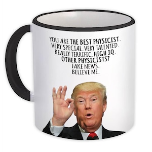 Puede incluir: Taza de cerámica blanca con asa y borde negros. La taza presenta un retrato de un hombre y el texto "YOU ARE THE BEST PHYSICIST. VERY SPECIAL. VERY TALENTED. REALLY TERRIFIC. HIGH IQ. OTHER PHYSICISTS? FAKE NEWS. BELIEVE ME."