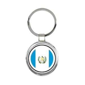 Puede incluir: Un llavero de plata con un dije redondo de plata que muestra la bandera de Guatemala. La bandera es azul, blanca y tiene el escudo nacional en el centro.