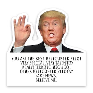 May include: A white sticker featuring a portrait of a man in a black suit and red tie, giving an "okay" hand gesture. Text on the sticker reads: "YOU ARE THE BEST HELICOPTER PILOT...FAKE NEWS. BELIEVE ME."