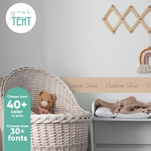 May include: A white wicker bassinet with a teddy bear inside. A tan wall with a beige banner that says "Custom Text Custom Text Custom Text" is behind the bassinet.