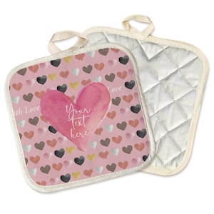 May include: Two square pot holders with cream-colored trim and hanging loops. One pot holder features a pink background with small hearts in various colors and a large pink heart with the text "Your Text Here". The other pot holder is quilted.