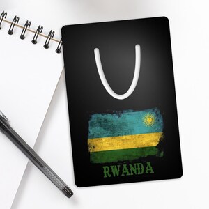 May include: A black bookmark with a white U-shaped cutout at the top. The bookmark features a distressed, faded image of the Rwandan flag with the word "RWANDA" printed below the flag.