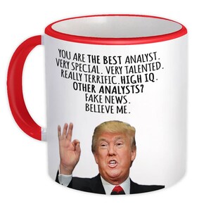 Op de afbeelding: Een witte koffiemok met een rode rand. De mok heeft een zwart-witte afbeelding van Donald Trump met de tekst "YOU ARE THE BEST ANALYST. VERY SPECIAL. VERY TALENTED. REALLY TERRIFIC. HIGH IQ. OTHER ANALYSTS? FAKE NEWS. BELIEVE ME."
