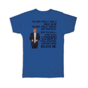 May include: Royal blue t-shirt featuring a graphic of a man in a suit with text. The text includes phrases like "LOSERS!" and "BELIEVE ME."