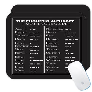 Op de afbeelding: Zwarte muismat met een witte rand met "THE PHONETIC ALPHABET - MORSE CODE GUIDE." De gids toont letters met hun Morsecode en fonetische alfabetwoorden. Een witte computermuis bevindt zich in de rechter benedenhoek.