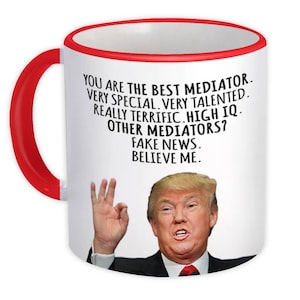 May include: White ceramic mug with a red handle and rim. The mug features a portrait of a man and text that reads "YOU ARE THE BEST MEDIATOR. VERY SPECIAL. VERY TALENTED. REALLY TERRIFIC. HIGH IQ. OTHER MEDIATORS? FAKE NEWS. BELIEVE ME."
