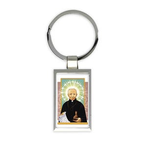 May include: Silver keyring with a rectangular image of a man in a black robe holding a scroll and a bottle. The image is surrounded by a white border and a halo of light.