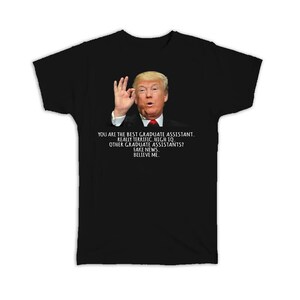 May include: Black t-shirt with a white graphic of Donald Trump making an OK sign. The text on the shirt reads "You are the best graduate assistant. Really terrific. High IQ. Other graduate assistants? Fake news. Believe me."