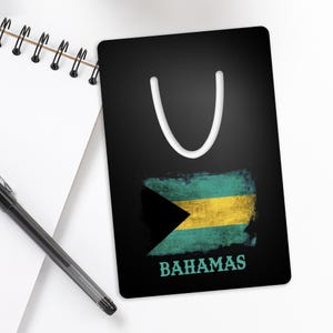 May include: A black bookmark with a white loop at the top. The bookmark features a distressed design of the Bahamas flag in teal, yellow, and black, with the word "BAHAMAS" in teal.