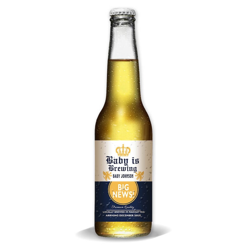 May include: A clear glass beer bottle filled with a golden liquid. The label reads "Baby is Brewing" with a crown graphic and "BIG NEWS!". The bottle has a silver cap and is against a white background.