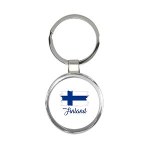 May include: A round, silver-colored keychain with a white background featuring the Finland flag and the word "Finland" in a cursive font. The flag is a blue cross on a white background.