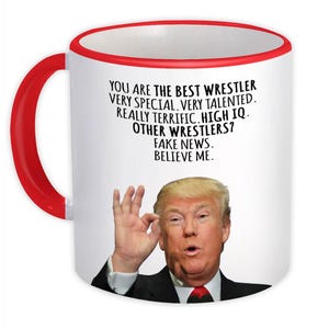 May include: White ceramic mug with a red handle and rim. The mug features a portrait of a man and text that reads "YOU ARE THE BEST WRESTLER...FAKE NEWS. BELIEVE ME."