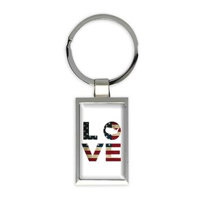 May include: Silver-toned metal keychain with a rectangular pendant. The pendant features the word "LOVE" in a distressed American flag design. The "O" is replaced with a map of the United States.