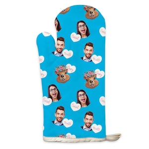 Könnte beinhalten: Ein blauer Ofenhandschuh mit einem sich wiederholenden Muster aus lächelnden Gesichtern, Cartoon-Murmeltieren mit Blumenkränzen und Namen in herzförmigen Sprechblasen. Mit weißem Besatz und einer Aufhängeschlaufe.