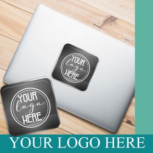 May include: Two black and white round stickers with the text "YOUR LOGO HERE" on a silver laptop. The stickers are on a wooden surface.