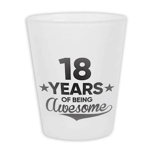 May include: A white shot glass with the text "18 YEARS OF BEING Awesome" in black. The number 18 is large and bold, with the word "YEARS" between two stars. The word "Awesome" is in a cursive font.