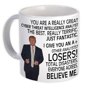 May include: White ceramic mug with a handle, featuring a portrait of a man in a suit and text that reads "YOU ARE A REALLY GREAT CYBER THREAT INTELLIGENCE ANALYST THE BEST. REALLY TERRIFIC. JUST FANTASTIC. I GIVE YOU AN A+ OTHER ANALYSTS? LOSERS! BELIEVE ME."